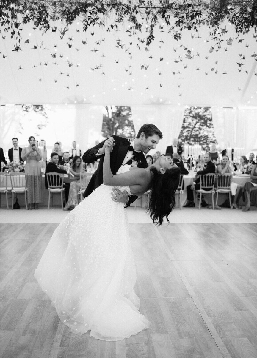 A pair of newlyweds share their first dance under an installation of origami cranes in the tent where their reception took place after their waterfront wedding ceremony.