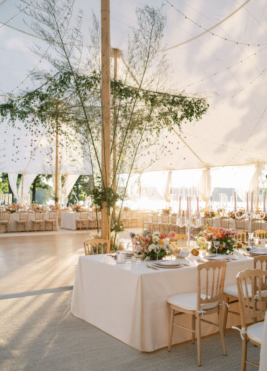 The tent was filled with glowing sunshine at the start of this waterfront wedding reception, which was set with long tables covered in a pale pink linen and elegant chairs.