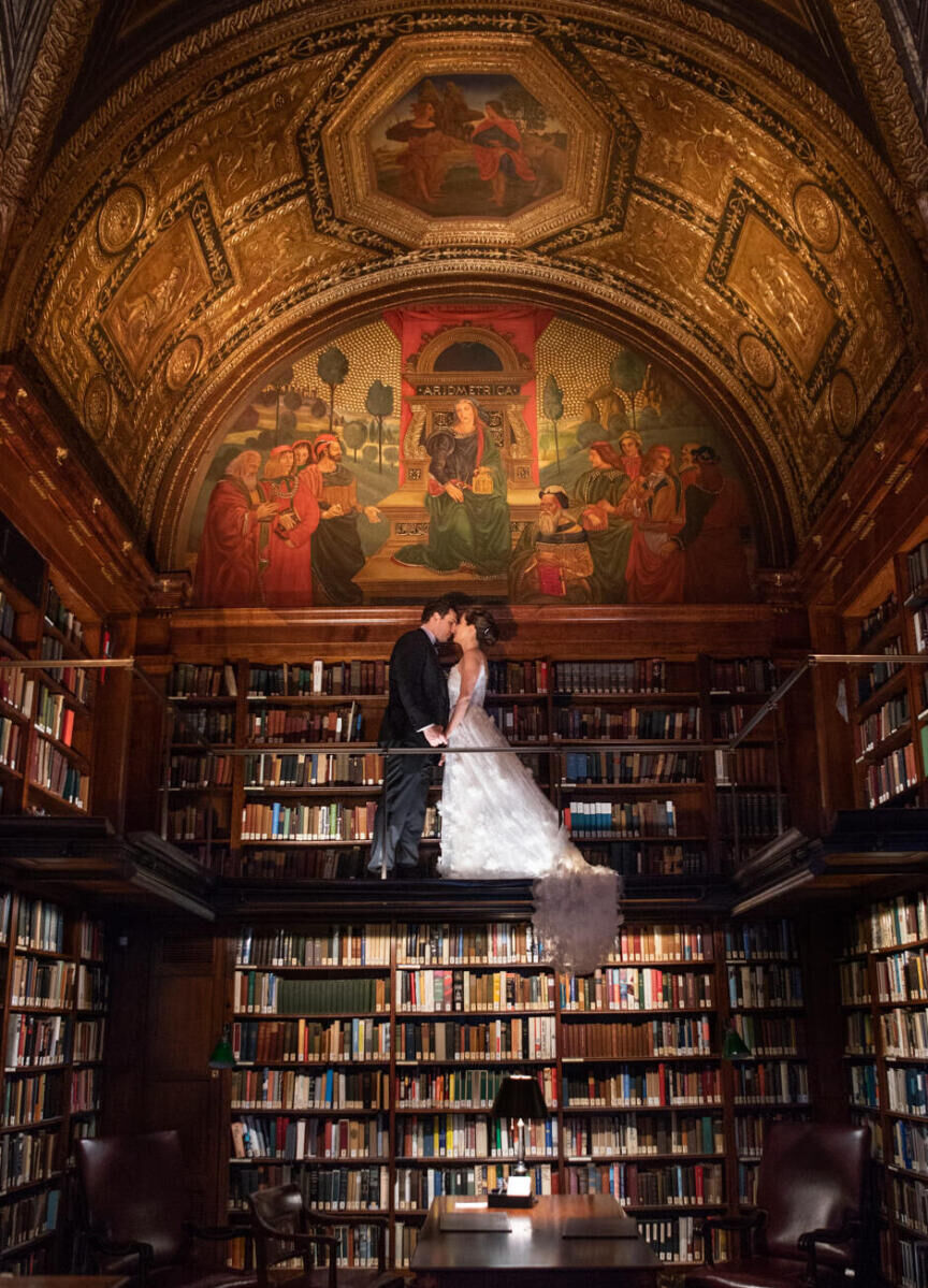 Wedding Photography Ideas: A bride and groom looking at each other while standing on a ledge at an opulent library.
