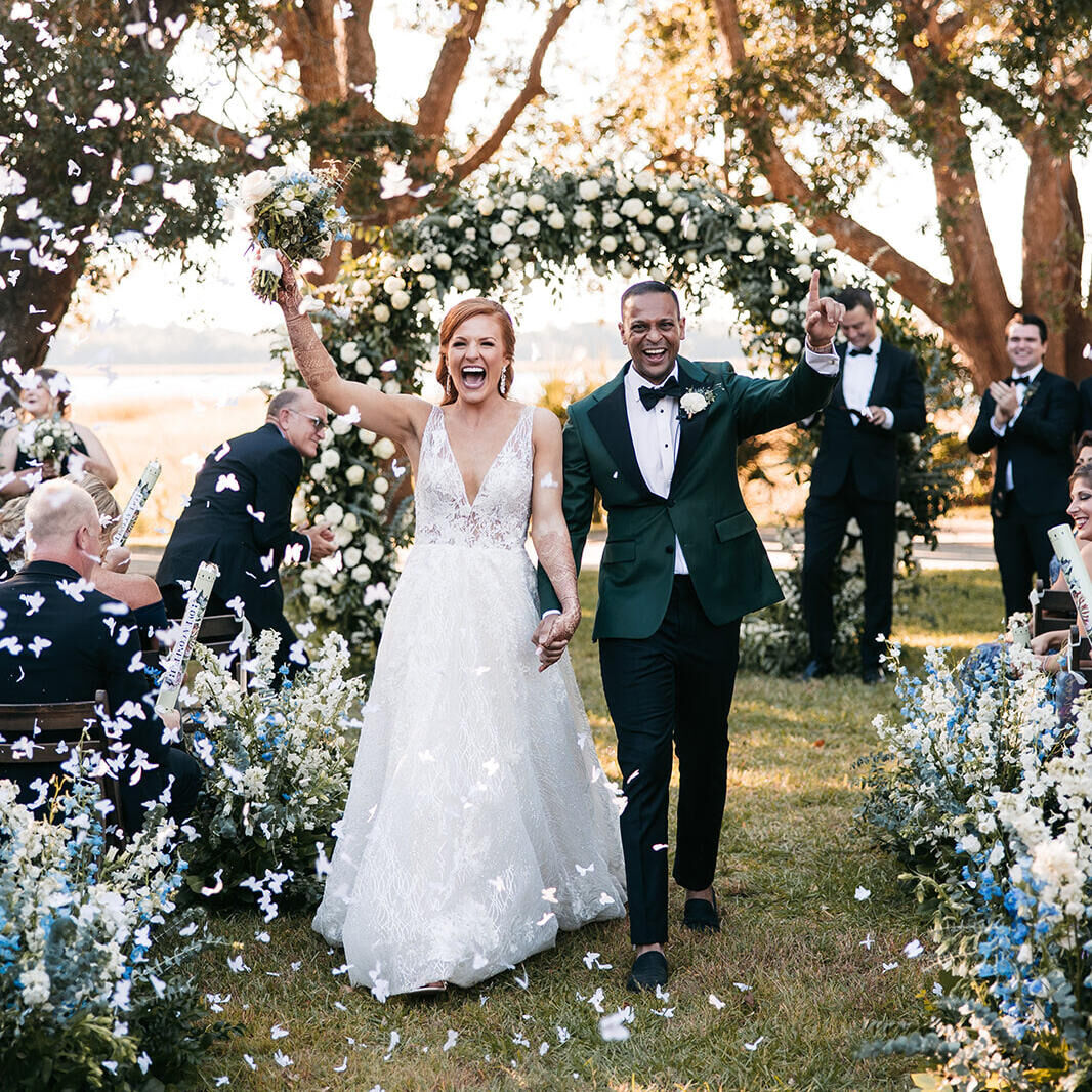 Wedding Tips: Two newlyweds cheering and walking back down the aisle together hand-in-hand, surrounded by confetti.