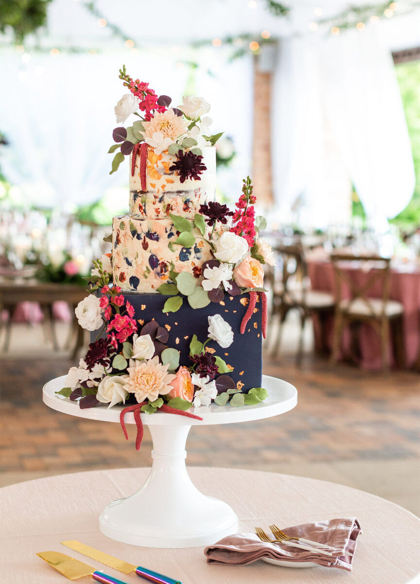 Wedding Tips: A three-tiered, super-colorful cake adorned with flowers. The cake is on a white stand atop a table, and there are colorful knives and forks on the table.