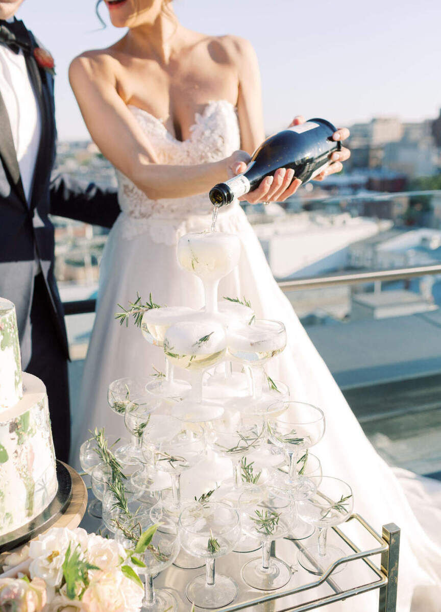 Wedding Tips: A bride pouring champagne over a tour of coupe glasses with rosemary garnishes.
