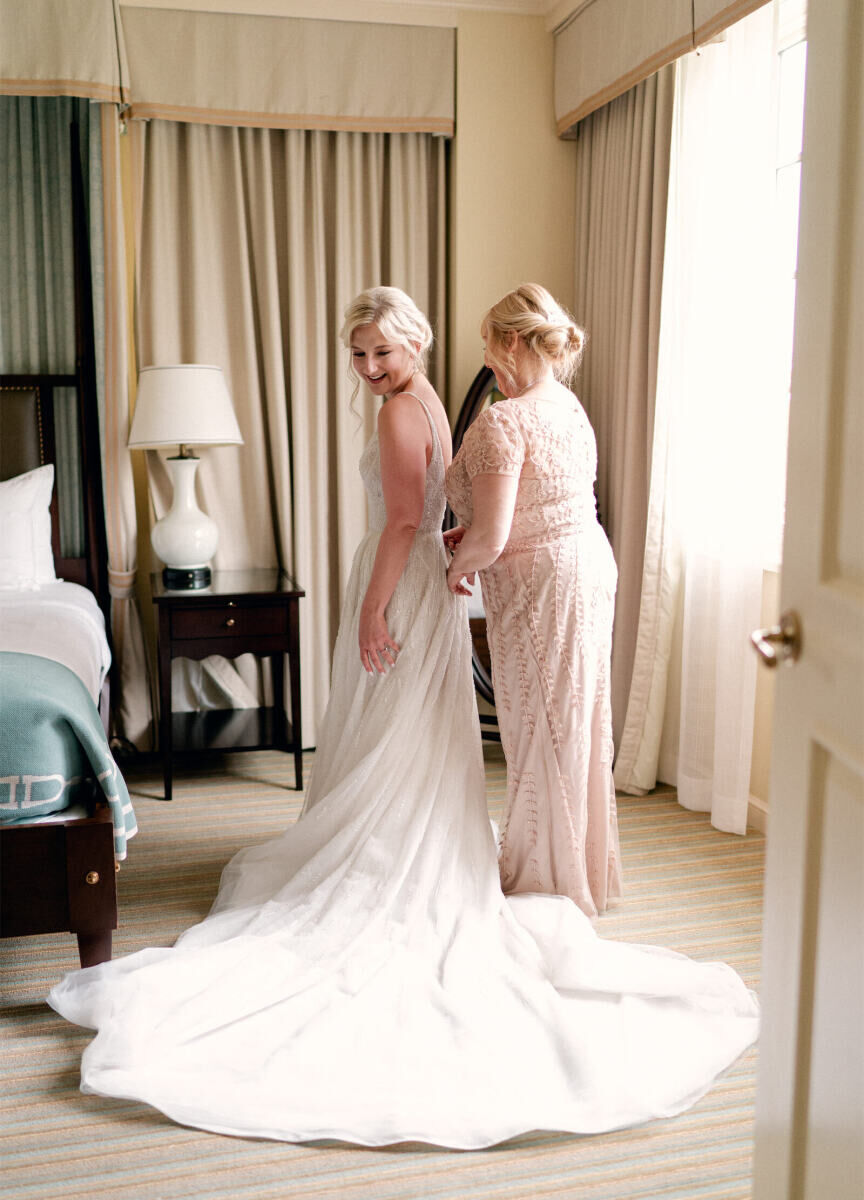 Wedding Tips: A woman who appears to be the bride's mom helping the bride zip into her wedding dress in a room.