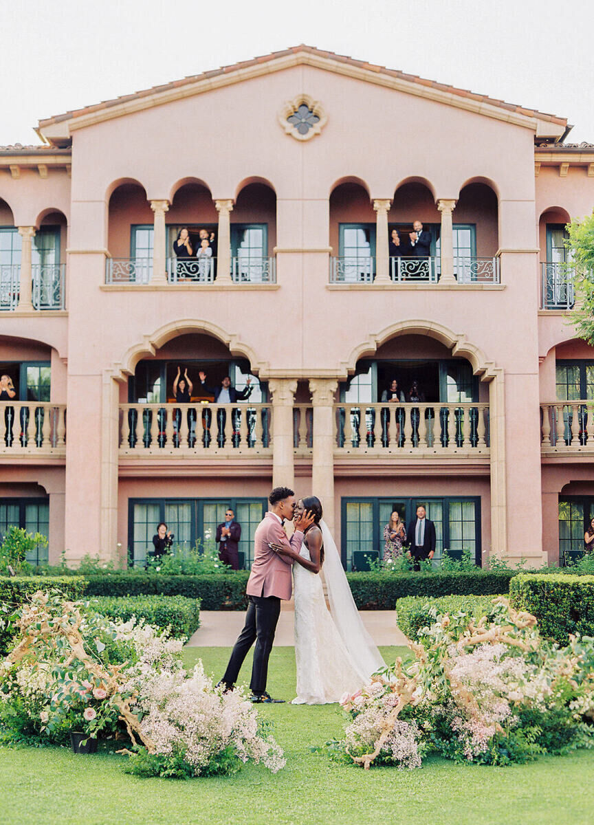 Wedding Tips: A bride and groom kissing after their ceremony while guests applaud from above and behind them at their venue.