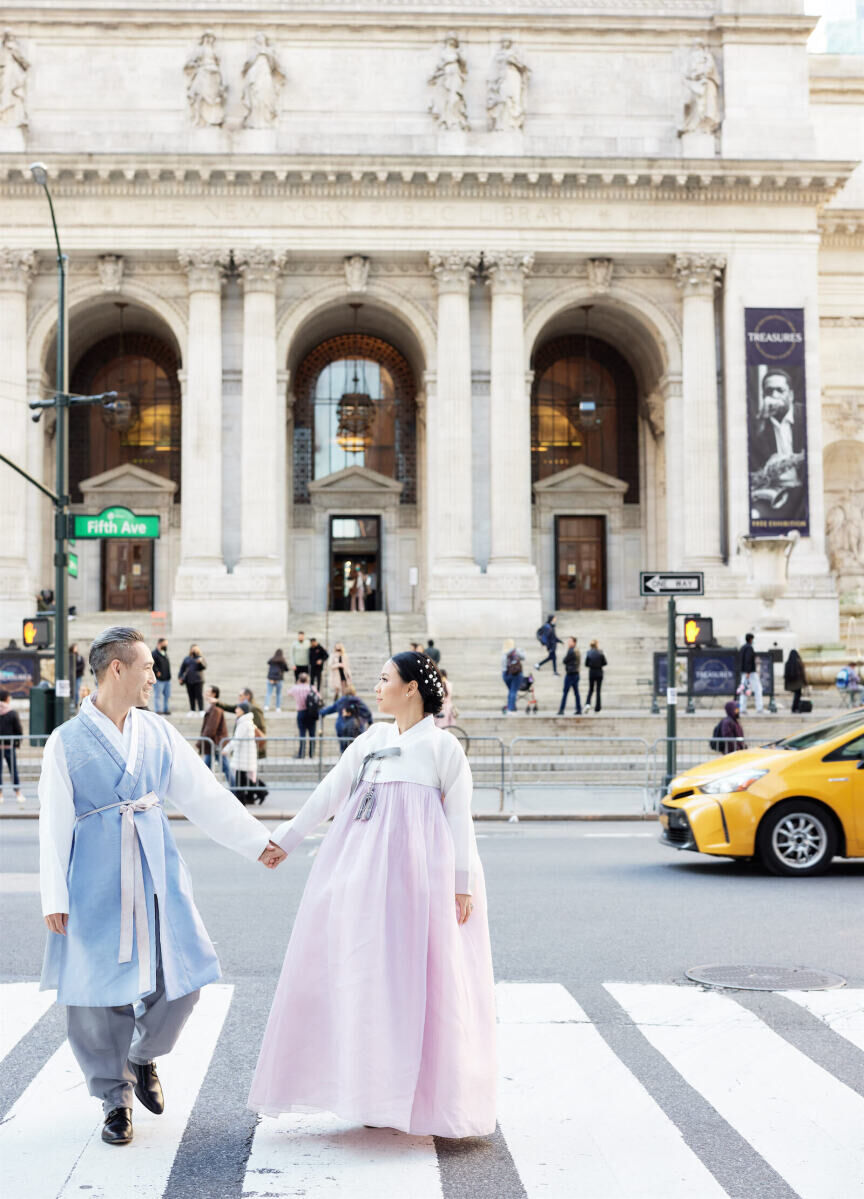 Wedding Tips: A bride and groom looking at each other and holding hands while standing in the crosswalk in front of New York Public Library.
