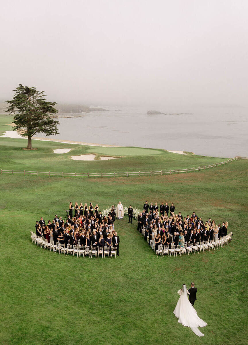 Wedding Tips: Drone footage of a bride being walked down the aisle at an outdoor venue near the water while guests watch.