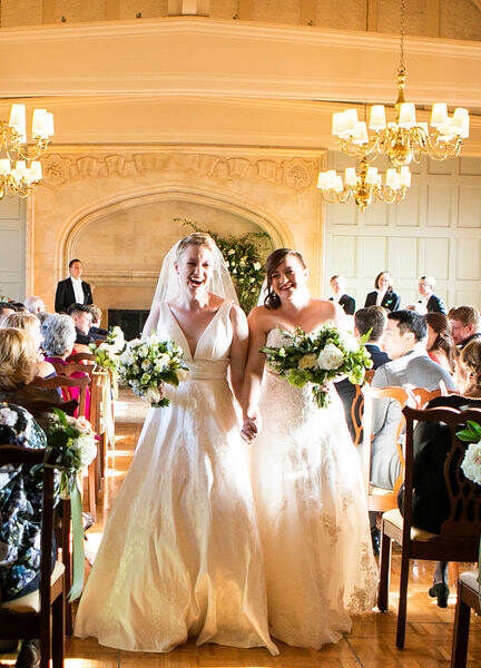 Two brides smiling and walking hand-in-hand back down the aisle together.