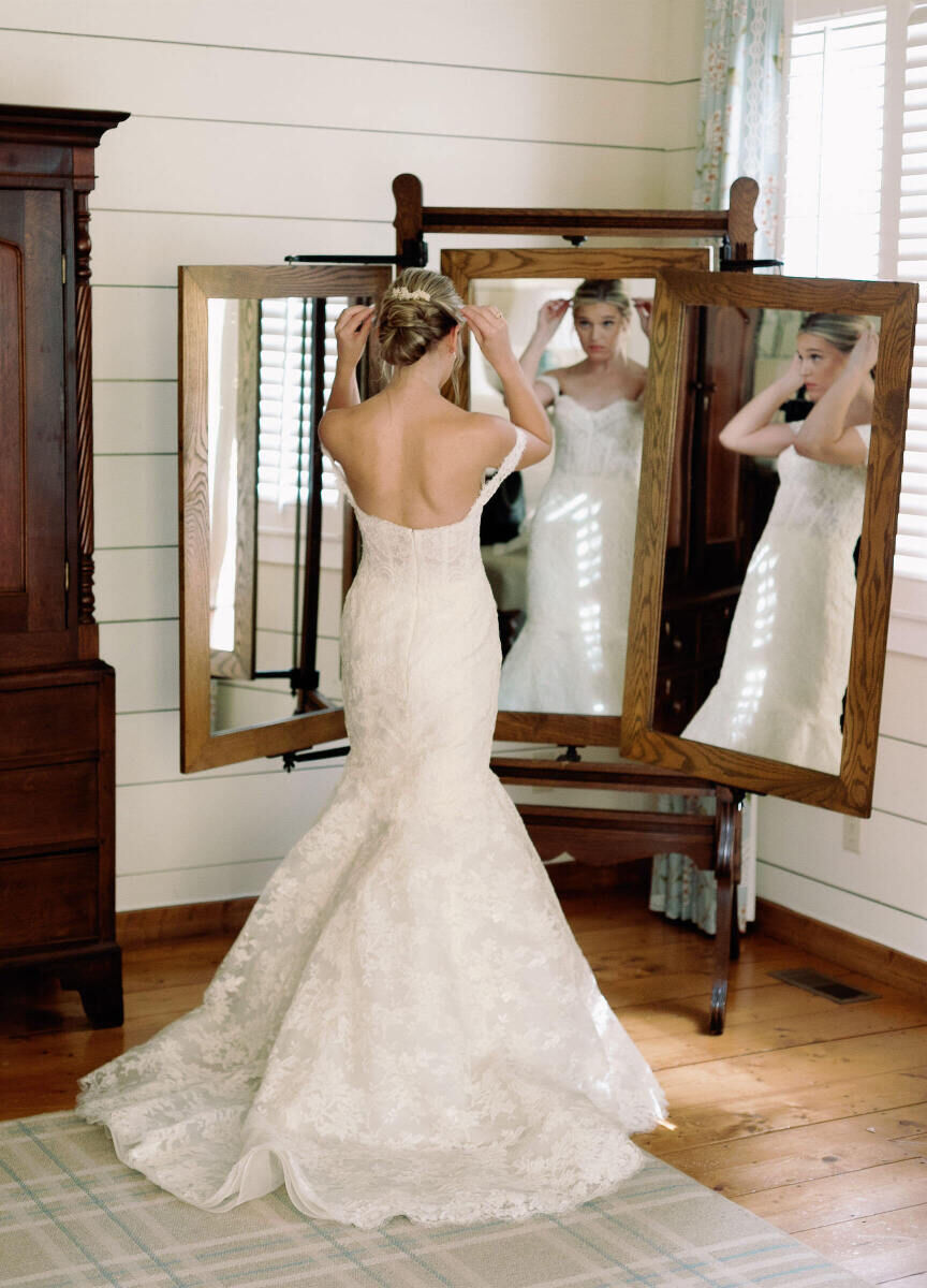 Wedding Tips: A bride in her wedding gown adjusting her hair in a three-way mirror.