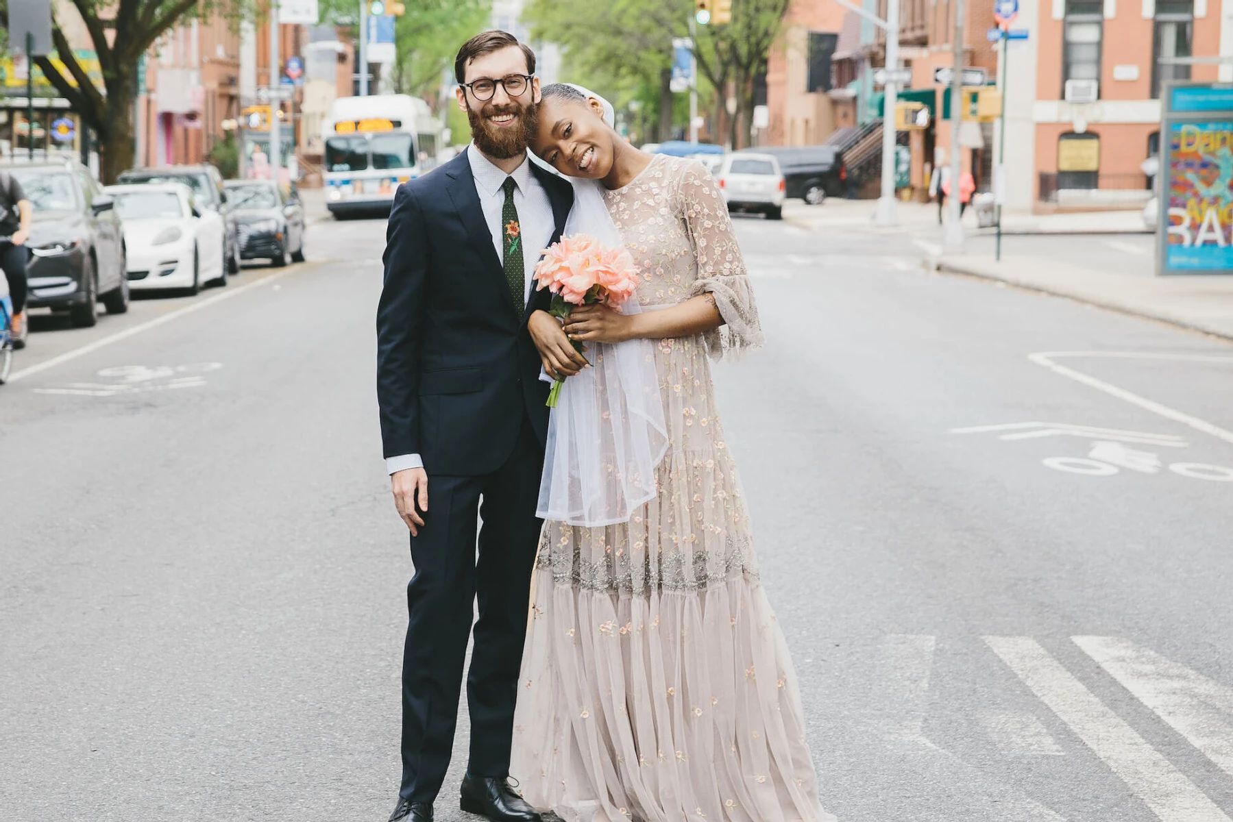 Wedding Tips: A bride smiling and resting her head on a groom's shoulder in the middle of a quiet city street on a sunny day.